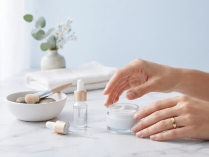 Hands reaching for a cream jar next to a dropper bottle on a white marble surface