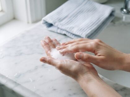 Hands working face wash into a soft foam over a marble sink