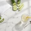 Aloe leaves, cucumber slices, a white towel and a glass of lemon water on a marble counter