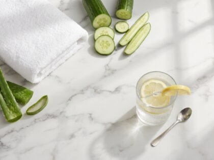 Aloe leaves, cucumber slices, a white towel and a glass of lemon water on a marble counter