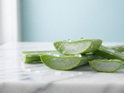 Fresh sliced aloe vera leaves with clear gel and water drops on a white marble counter